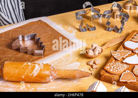 Weihnachts-Lebkuchen in verschiedenen Formen mit Zuckerguss und Zutaten für Lebkuchen auf Holztisch, Nahaufnahme mit selektivem Fokus Stockfoto