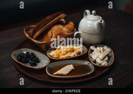 Traditionelles türkisches Frühstück mit Spiegelei, schwarzen Oliven, Croissant, Brot, Käse, Butter in Honig und Tee auf einem Holztisch. Bio, frisch und ta Stockfoto