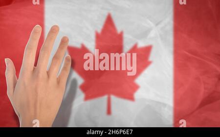 Eine Frauenhand auf dem Hintergrund der Nationalflagge Kanadas. Eine Geste mit erhobener Hand vor dem Hintergrund der kanadischen Flagge. Stockfoto