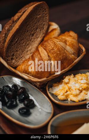 Traditionelles türkisches Frühstück mit Spiegelei, schwarzen Oliven, Croissant, Brot, Käse, Butter in Honig und Tee auf einem Holztisch. Bio, frisch und ta Stockfoto