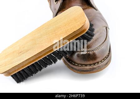 Alte braune Lederschuhe mit Paste poliert, Schuhbürste liegt auf dem Schuh, isoliert auf weißem Hintergrund.
