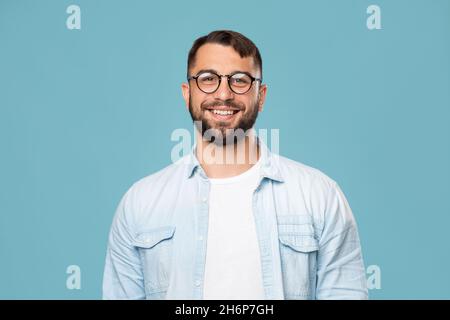 Lächelnder, freundlicher, reifer kaukasischer Mann in einer Brille, der auf blauem Hintergrund isoliert auf die Kamera schaut Stockfoto