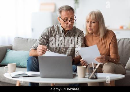 Seniorenpaar Schaut Sich Die Papiere An Und Zählt Rechnungen Zu Hause Lesen Stockfoto