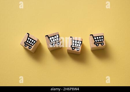 Holzwürfel mit den Warenkorb-Icons auf gelbem Hintergrund - Einkaufskonzept Stockfoto