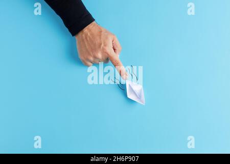 Männliche Hand schiebt ein Papier-Origami-Boot auf blauem Hintergrund nach vorne. Konzept für Partnerschaft, Beratung, Unterstützung, Führung oder geschäftliche Teamarbeit. Stockfoto