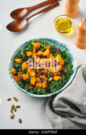 Herbstsalat mit Grünkohl, geröstetem Kürbis, Samen und getrockneten Preiselbeeren in einer Schüssel. Grauer Hintergrund. Modell. Draufsicht. Stockfoto