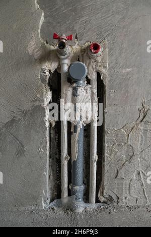 In der Betonwand befinden sich drei Kunststoffrohre. Zwei für kaltes und warmes Wasser. Die dritte für Abwasser. Ein Rohr mit einem Wasserhahn, das andere mit Stopfen. T Stockfoto