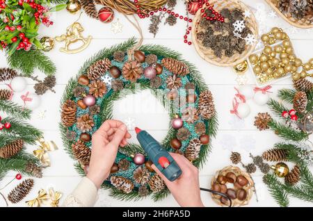 Schritt für Schritt einen großen Weihnachtskranz machen, Schritt 12 - kleine dekorative Plastikschneeflocken nehmen und mit heißem Kleber kleben Stockfoto