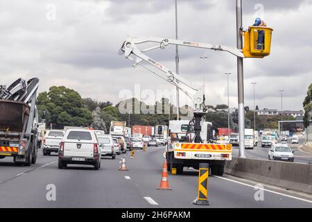 Johannesburg, Südafrika - 8. Juni 2021: Die Autobahnbeleuchtung wird durch das Arbeitspersonal ersetzt. Kirschpflücker mit Mann, der das Licht wechselt. Stockfoto