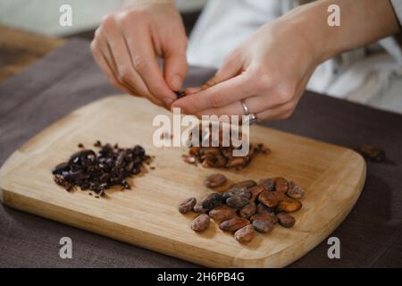 Hände schälen Bio-Kakaobohnen auf Holztisch, Kakaobohnen, handwerkliche Schokolade in rustikalem Stil für die Zeremonie auf dem Tisch. Degustation Stockfoto