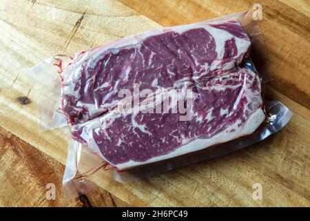 Fresh Raw New York Strip Beef Steaks vakuumverpackt in Kunststoff auf Holzoberfläche Stockfoto