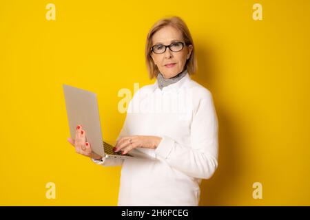 Ältere Frau hält Laptop isoliert über gelben Hintergrund. Stockfoto