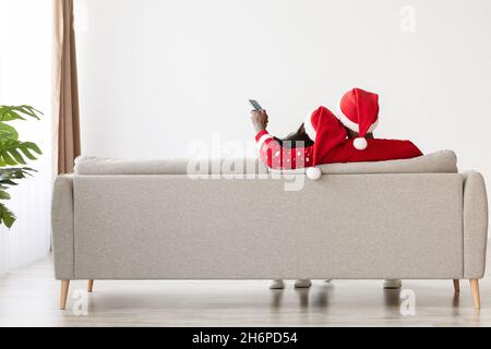 Unbekanntes schwarzes Paar, das zu Hause auf dem Sofa sitzt und die Fernbedienung hält Stockfoto