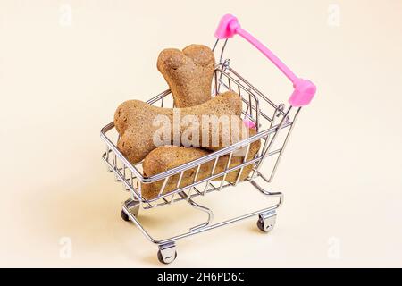 Braune Keksknochen für Hunde im Trolley-Warenkorb auf hellem Hintergrund. Hunde- und Welpenfutter, gesunde Leckereien Verkauf. Stockfoto