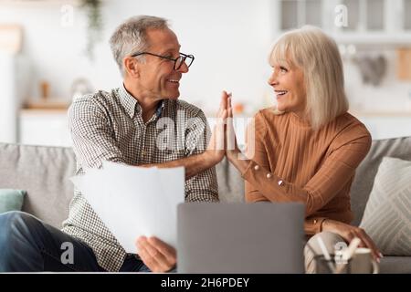 Glückliches Senior-Paar, Das High-Five-Papiere Beim Lesen Von Rechnungen In Der Halle Gibt Stockfoto