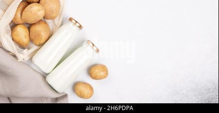 Vegane Milch auf pflanzlicher Basis in zwei Flaschen. Alternative Kartoffelmilch und Kartoffelknollen auf grauem Tisch. Draufsicht. Kopierbereich - Bild Stockfoto