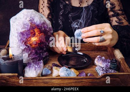 Glamouröse Frau im schwarzen Kleid reinigt Kristalle Edelsteine durch verschmierenden Palo Santo Holzstab. Entfernen Sie negative Energie. Stockfoto