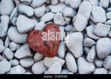 Ein geschnitztes / geformtes Herz aus einem Stück Granitstein auf einem Hintergrund aus weißen Felsen. Liebe, Romantik, Romantik Stockfoto