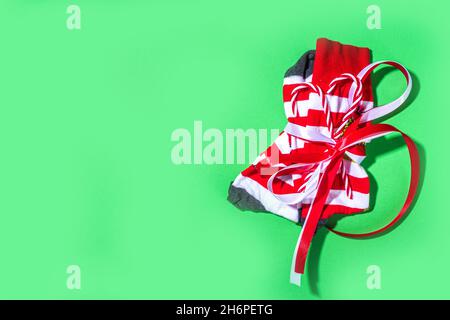 Weihnachtsstile rot weiß gestreifte Socken verpackt als Geschenk mit festlichem Band und Zuckerrohr Dekorationen. Niedliches modernes Trend-Weihnachtsgeschenk für das neue Jahr Stockfoto
