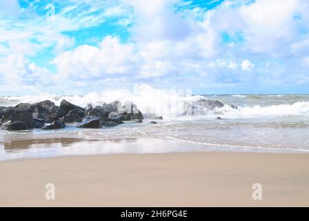 Meereswellen brechen auf Steinen und Felsen in der Nähe von Sandy Beach. Spritzwasser Salzwasser bildet Schaum in der Nähe von Empty Coast, Lemvig, Dänemark, Frühjahr 2016. Stockfoto