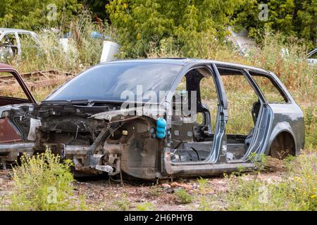 Demontierte Karosserieteile im Grünen im Freien aufgegeben. Autodumpe, Wrack auf einem Schrottplatz, bereit zum Recycling Stockfoto