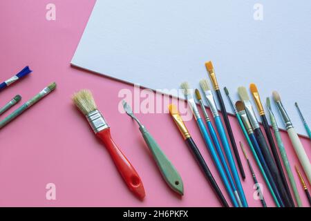 Pinsel und weiße Leinwand auf rosa Papier Hintergrund. Bildung, Schule und Kunstkonzept. Freier Speicherplatz für Text oder Bild Stockfoto