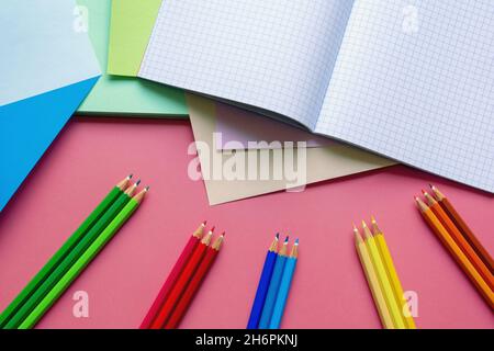 Schule und Hobby Konzepte. Farbige Papierblätter, Buntstifte und Notizbuch auf rosa Papierhintergrund. Freier Speicherplatz für Text Stockfoto