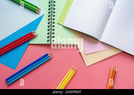 Schule und Hobby Konzepte. Farbige Papierblätter, Buntstifte und Notizbücher auf rosa Papierhintergrund. Speicherplatz kopieren Stockfoto