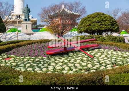 Busan, Südkorea - 28. November 2015: Blumenuhr auf Hintergrund Statue von Yi Sun-Sin und Busan Turm. Stockfoto