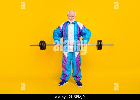 Foto in voller Länge von pensionierten Mann, der körperliche Übungen mit Langhantel auf gelbem Hintergrund ausgeführt hat Stockfoto