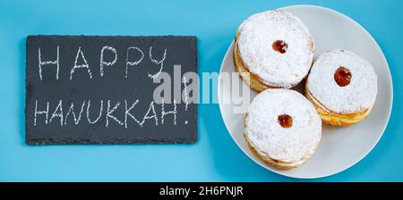 Frohes Chanukka. Jüdische Dessert sufganiyot Donuts auf blauem Hintergrund. Symbol des religiösen Judentums Feiertag. Beschriftung auf der Kreidetafel. Stockfoto