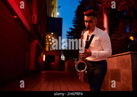 Der junge Saxophonist spielt nachts auf der Straße den Sax Stockfoto