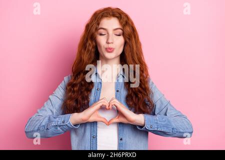 Foto von flirty ziemlich junge Dame gekleidet Jeans lächelnd zeigt Finger Herz senden Sie isoliert rosa Farbe Hintergrund küssen Stockfoto