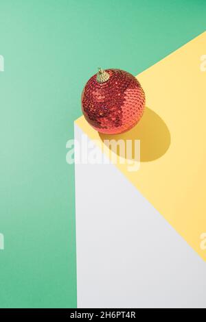 Vintage minimalistisches geometrisches Konzept mit roter Weihnachtskugel auf weißem, gelbem und mintgrünem Hintergrund. Kreative Schwerkraft Anordnung. Silvesterparty c Stockfoto