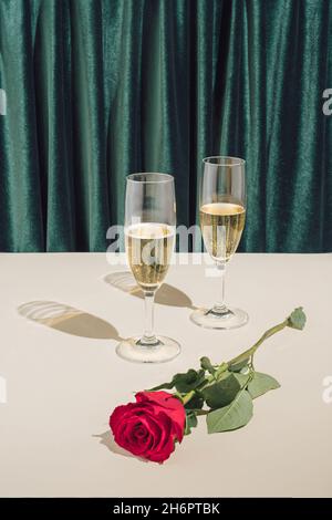 Minimal romantische 2022 Neujahr oder Weihnachtsfeier Komposition. Kreative Vintage-Art-Regie mit Sektgläsern und roter Rose. Stockfoto