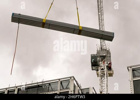 London, England - August 2021: Die Ladung von Stahlbaumaterialien wird von einem Turmdrehkran auf die Spitze eines im Bau befindlichen Neubaus gehoben Stockfoto