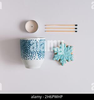 Winterkomposition mit Teetasse, Schneeflockenkeks, Streichhölzern und Kerze. Minimal flach lag auf weißem Hintergrund. Stockfoto