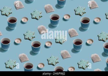 Wintermuster aus Teebeutel, Tasse, Kerze und Schneeflockenkeks auf pastellblauem Hintergrund. Minimale Konzeptanordnung. Stockfoto