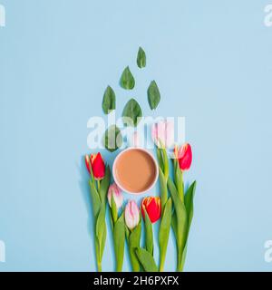 Kreative Frühlingsflachlage aus rosa und roten Tulpen, grünen Blättern und einer Tasse Kaffee. Minimale Pastelltöne. Stockfoto