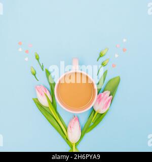 Kaffeetasse umgeben von grünen Blättern, Rosenknospen, rosa Herzen und Tulpen auf pastellblauem Hintergrund. Minimales Federkonzept. Stockfoto