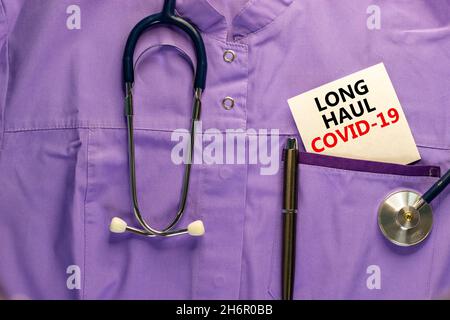 COVID-19 Symbol für langstreckige kovide Symptome. Weiße Karte mit den Worten Langstrecke covid-19. Medizinische Uniform, metallischer Stift und Stethoskop. Medizinisch, COVID-19 lo Stockfoto