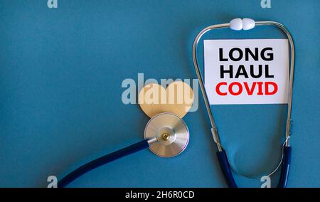 COVID-19 Symbol für langstreckige kovide Symptome. Weiße Karte mit Worten Langstrecke covid. Holzherz, Stethoskop, schöner blauer Hintergrund, Kopierraum. Mittel Stockfoto