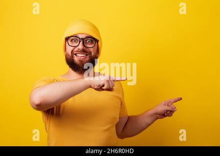 Lächelnder bärtiger Mann in einer Brille zeigen Zeigefinger auf gelben Hintergrund Stockfoto