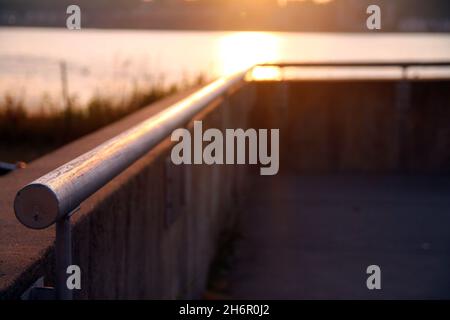 Nahaufnahme und Perspektive eines Handlaufs als Schutz über dem Fluss bei Sonnenuntergang Stockfoto