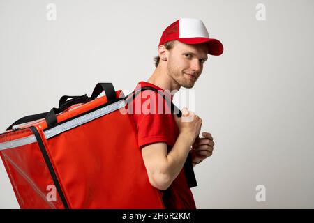 Seitenansicht Lieferung Mitarbeiter Mann 20s in roter Kappe T-Shirt uniform thermische Lebensmitteltasche Rucksack Arbeit Kurierdienst. Stockfoto