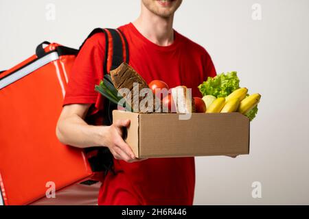 Lieferkonzept - schöner Liefermann, der eine Verpackung mit Lebensmitteln und Getränken aus dem Laden trägt. Stockfoto