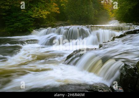 Lange Exposition von sich bewegenden Wasserströmen der Wasserfälle bei Bond Falls (Upper Falls) in der Nähe von Paulding, Michigan während des Herbstes bei Sonnenaufgang Stockfoto