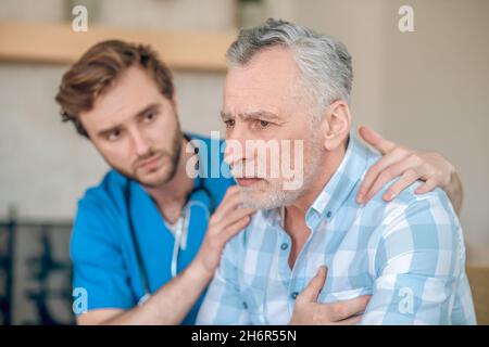 Aufmerksamer Kardiologe, der einen verängstigten kranken Mann unterstützt Stockfoto