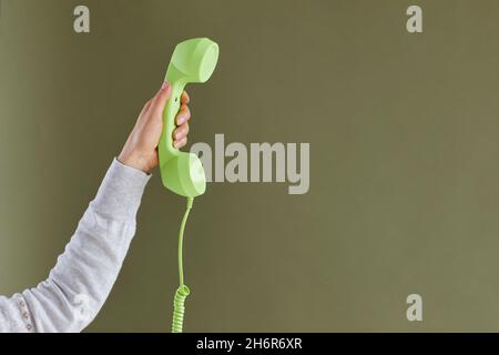 Die Hand der Frau hält einen hellgrünen Festnetzempfänger auf dem Hintergrund des Kopierbereichs Stockfoto