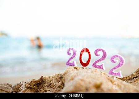 Abbildungen 2022 vor dem Hintergrund von Küstenwellen durch Meer oder Meer mit Karamellrohr. Reisen Sie während der Quarantäne am Silvesterabend vor dem Hintergrund Stockfoto